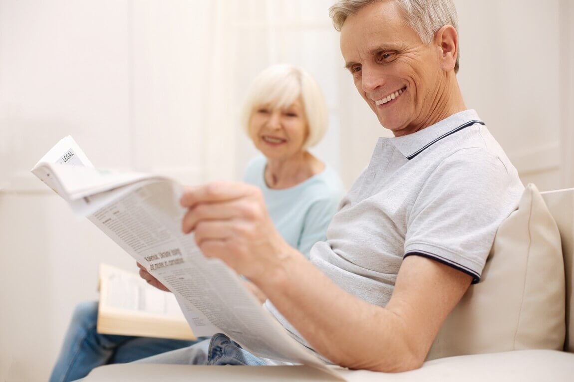 пожилой мужчина читает свежую газету и выглядит довольным