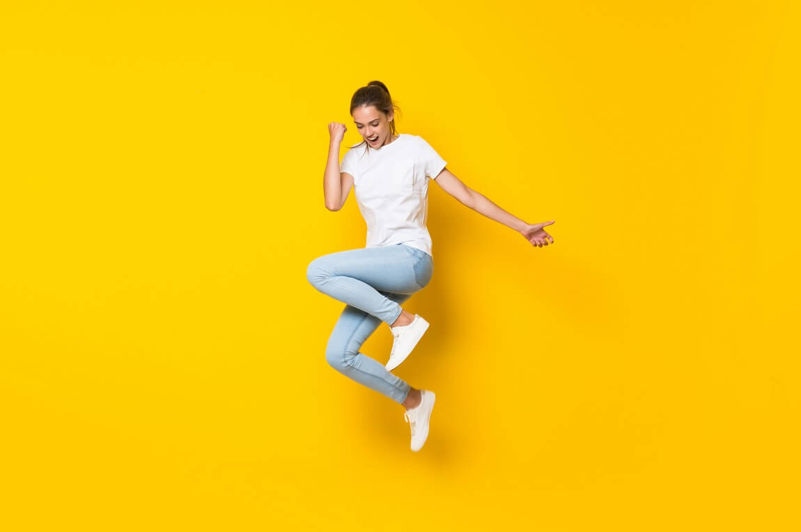 Молодая женщина прыгает через изолированную желтую стену