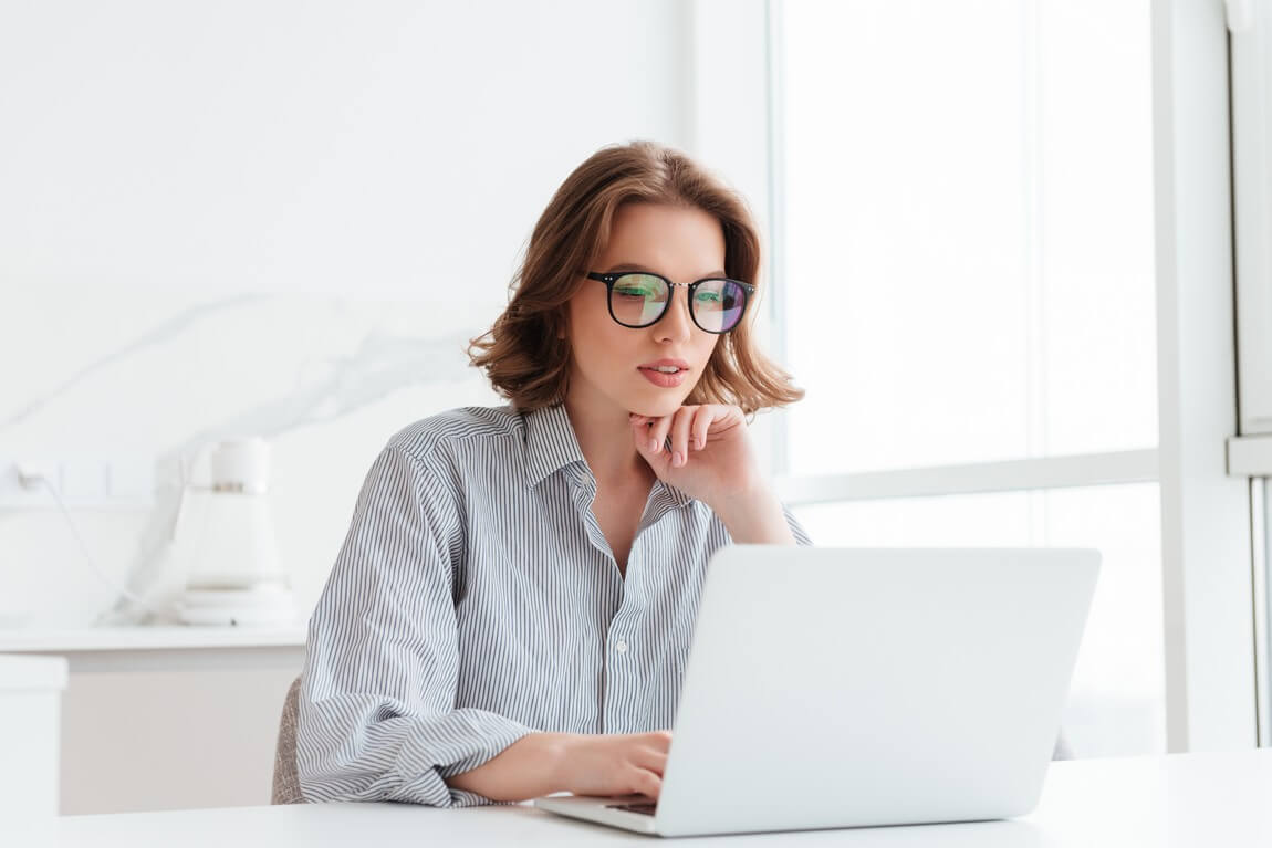 Очаровательная бизнесвумен в очках и полосатой рубашке работает с портативным компьютером